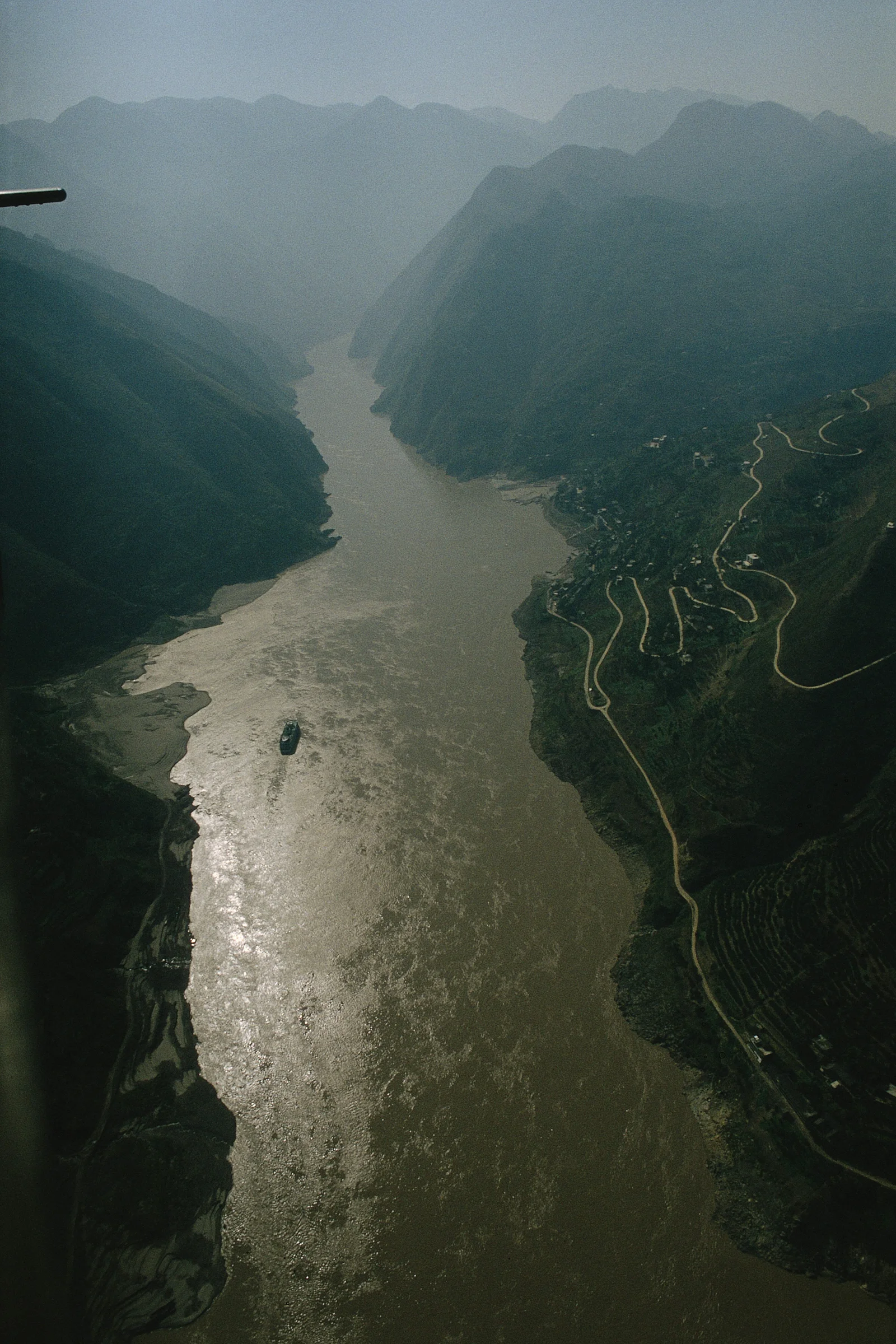 航拍视角展现一条河流穿过群山峡谷，山坡上可见蜿蜒道路。