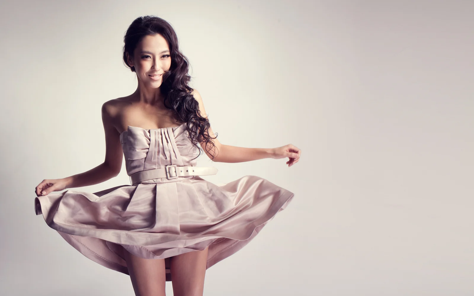 연한 분홍색 튜브톱 드레스를 입은 성인 여성이 밝은 배경 앞에서 포즈를 취하고 있습니다.