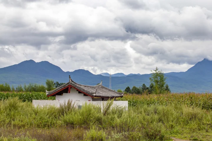 云层低垂的群山、田野与一座传统屋顶建筑构成宁静的自然风景。