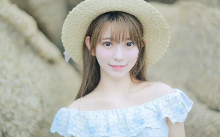 麦わら帽子をかぶった成人女性が屋外でカメラに向かって微笑んでいます。