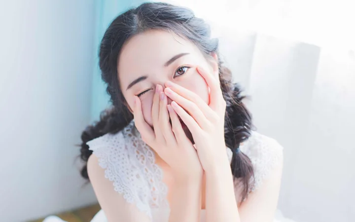一名女性在明亮的室内用双手遮住嘴巴微笑。