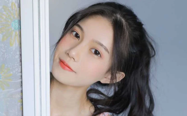 一名黑发女性靠在白色门框旁，面向镜头微笑。
