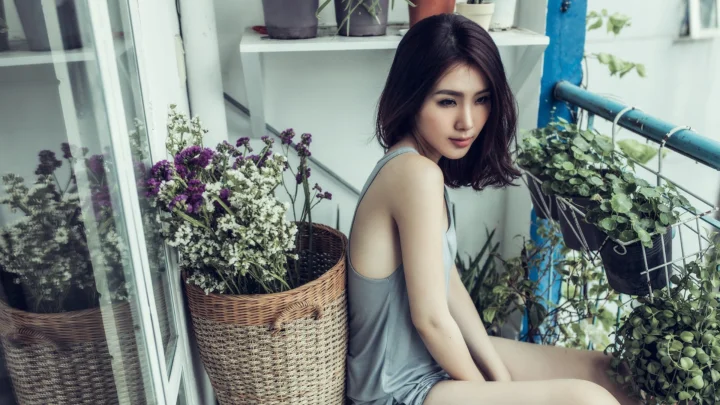 一名成年女子坐在摆满盆栽和花篮的阳台上。
