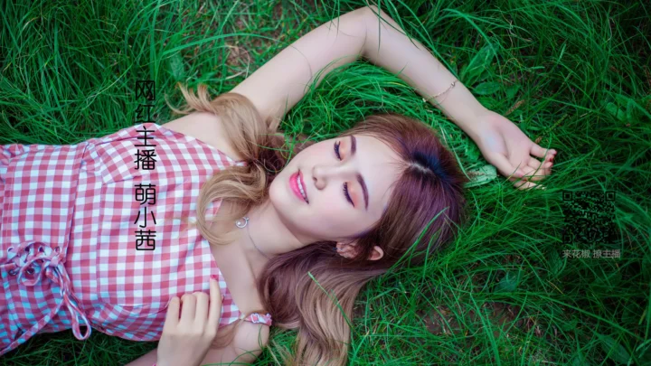 一名成年女子穿着粉白格纹裙躺在绿色草地上。