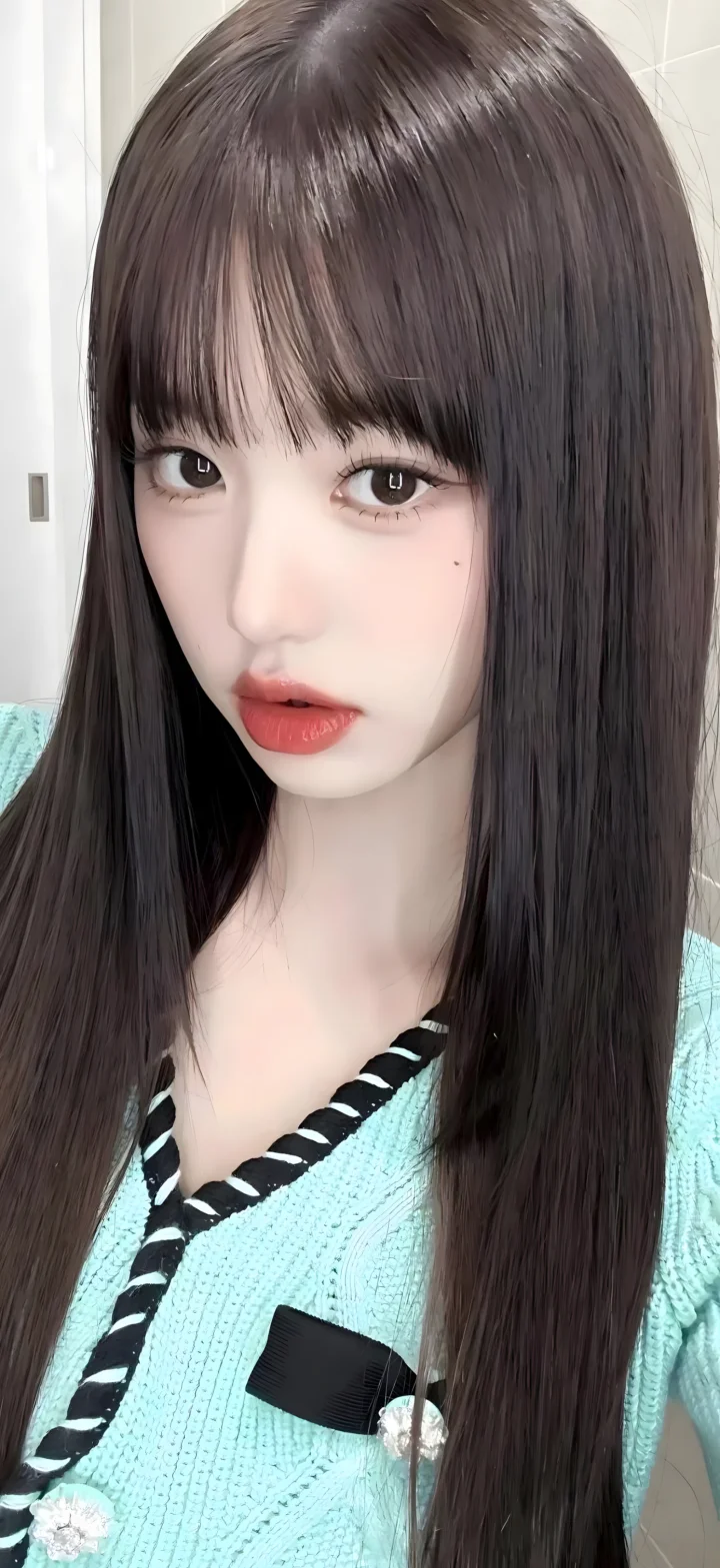 長い髪の女性が淡いターコイズ色のニットを着て室内でカメラを見つめています。