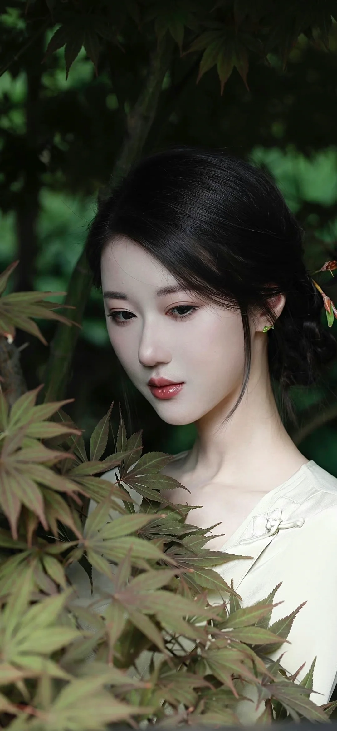 一位女性置身绿叶之间，身穿浅色上衣，面向侧前方。