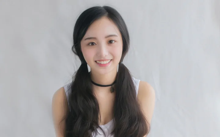 연한 회색 배경 앞에서 성인 여성이 카메라를 향해 미소 짓고 있습니다.