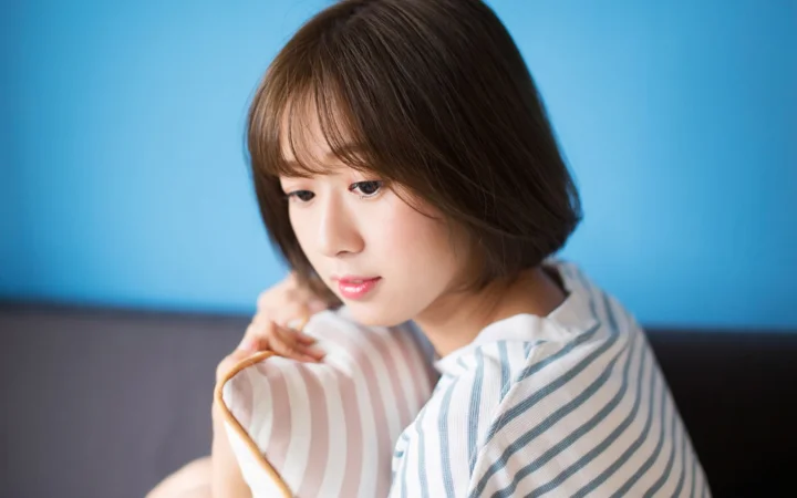 짧은 머리의 여성이 파란 배경 앞에서 연한 줄무늬 쿠션에 기대고 있다.