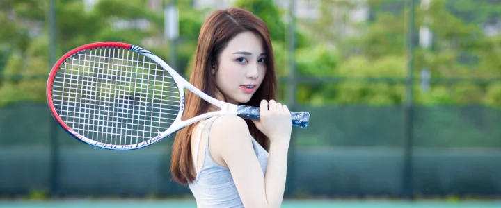 一名女子手持网球拍站在户外网球场前。