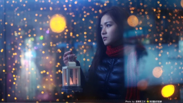 一名戴红色围巾的女子手提灯笼，站在五彩斑斓的虚化灯光前。