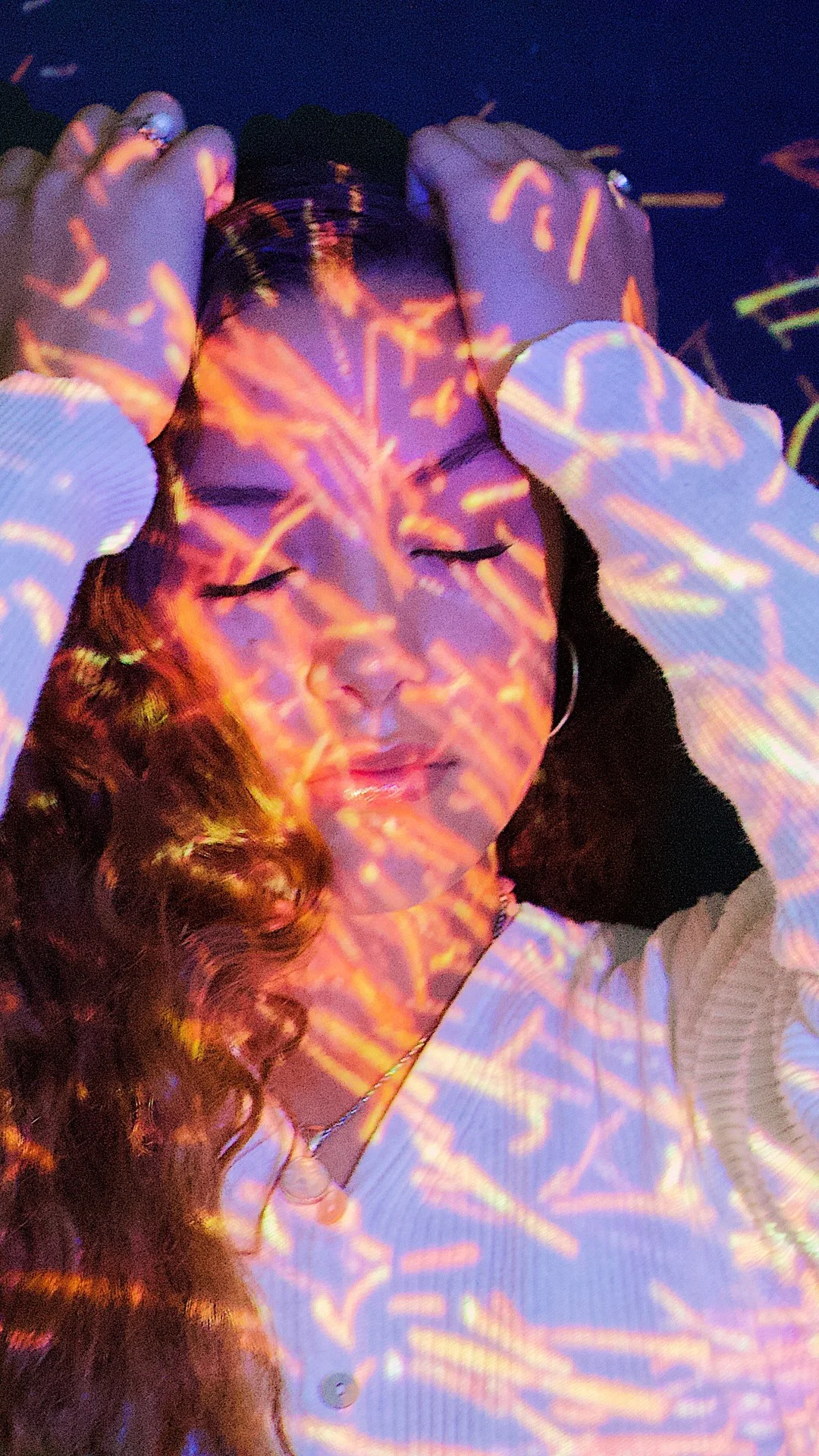 一位成年女性閉著眼睛舉起雙手，臉部和白色上衣上覆蓋著彩色光影圖案。