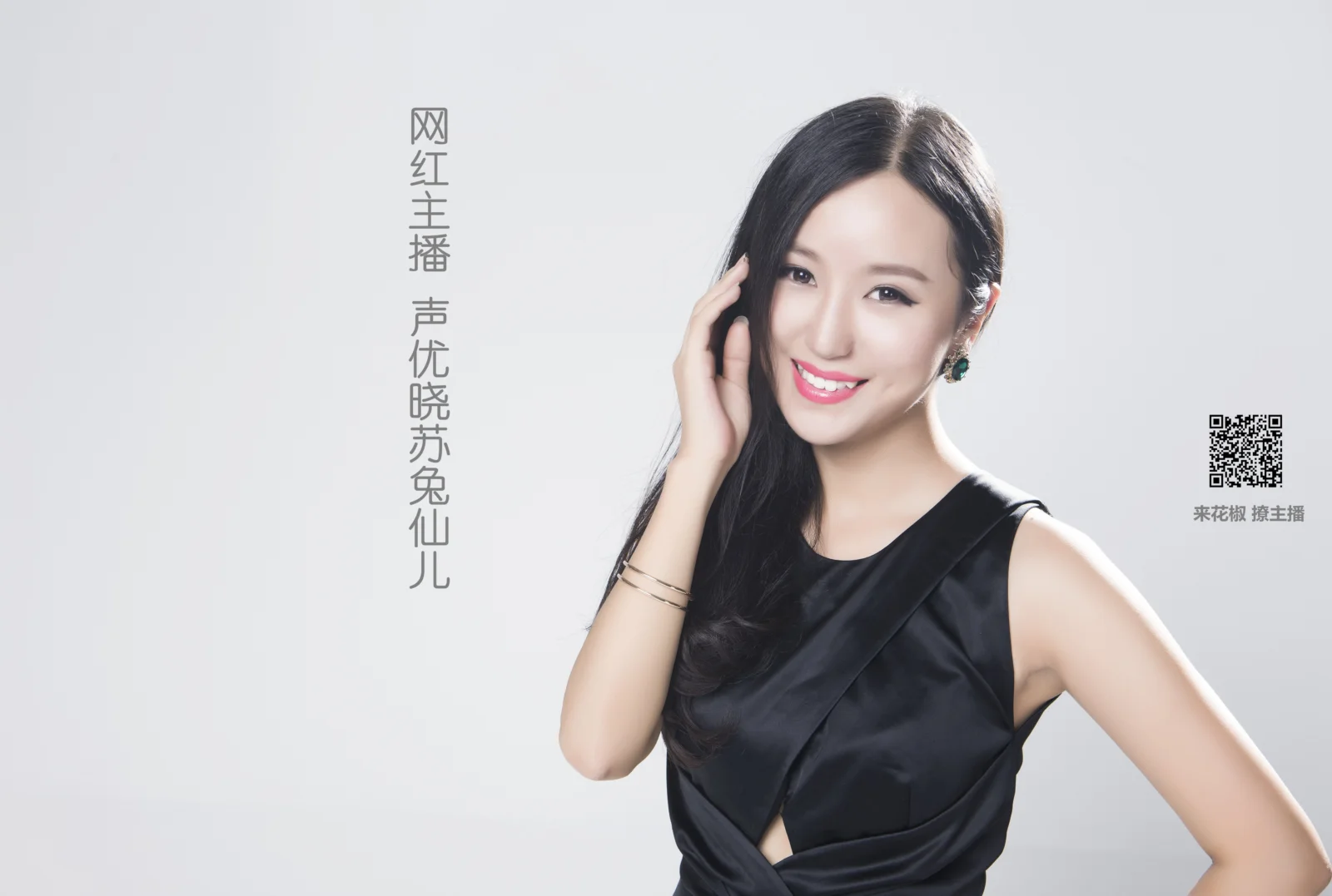 一名微笑的成年女性穿着黑色连衣裙，站在浅灰色背景前。