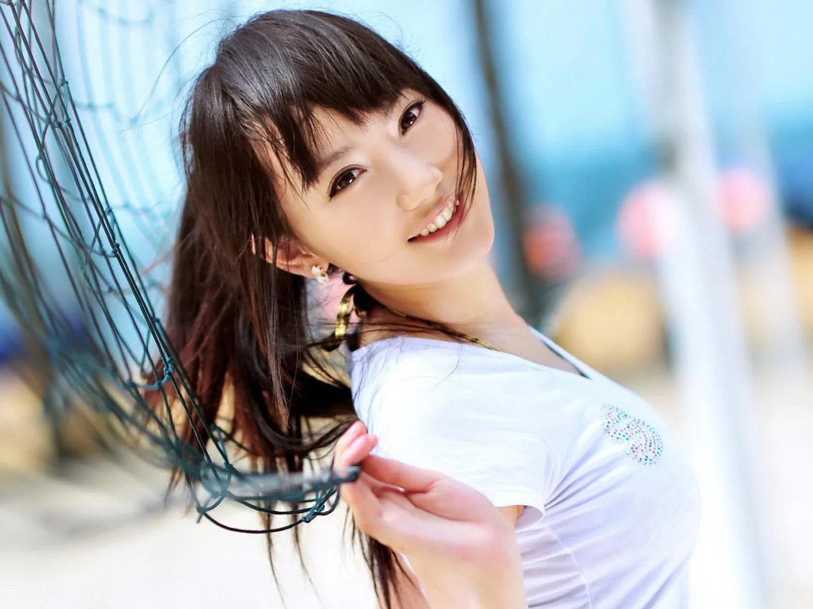 一名长发女性穿着白色上衣，微笑着站在网状设施旁。