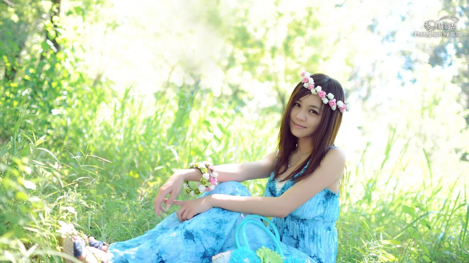 一名戴着花环、身穿蓝色连衣裙的女子坐在阳光洒落的绿色植被中。