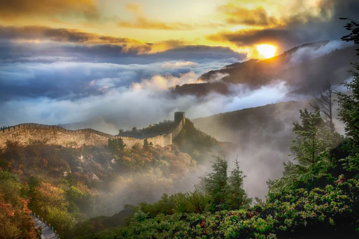 长城蜿蜒穿过山脊，云雾、群山与落日构成壮丽的风景画面。