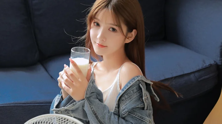 一名成年女性坐在深色沙发上，手持一杯饮品。