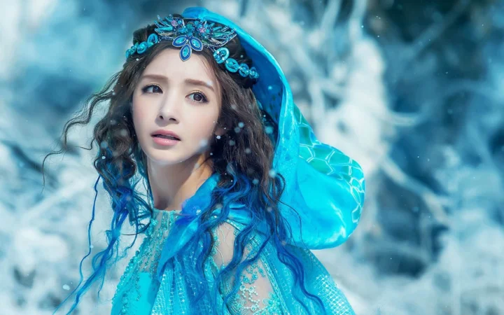 一名戴着宝石头饰、身穿蓝色服饰的女子置身于朦胧的雪景背景中。