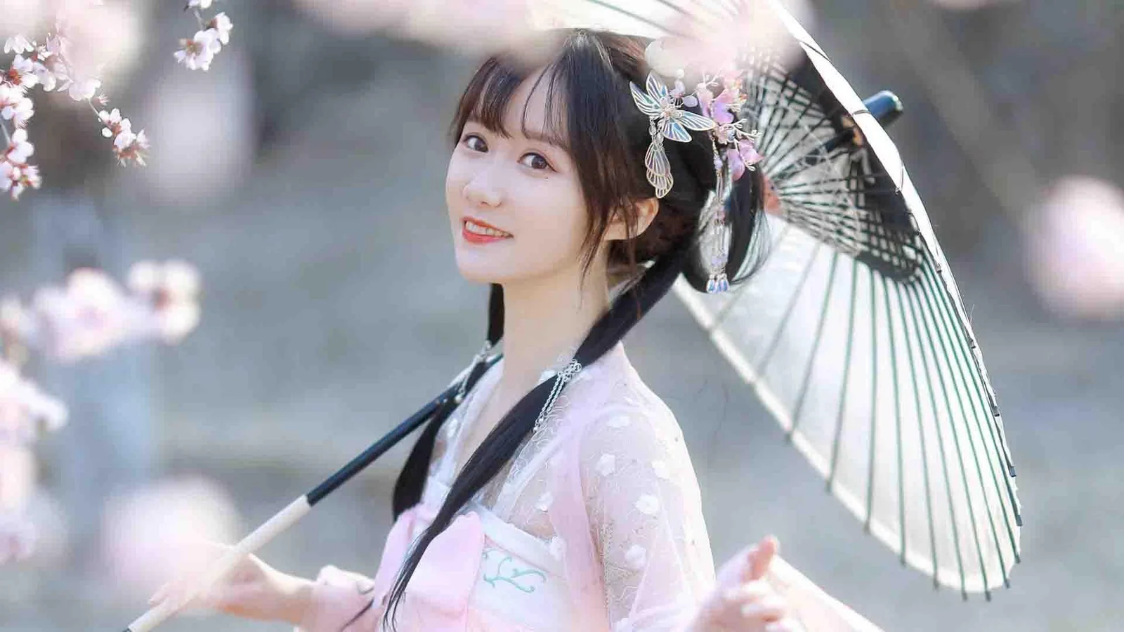 一位身穿浅色传统服饰的女子在花枝与纸伞前微笑。