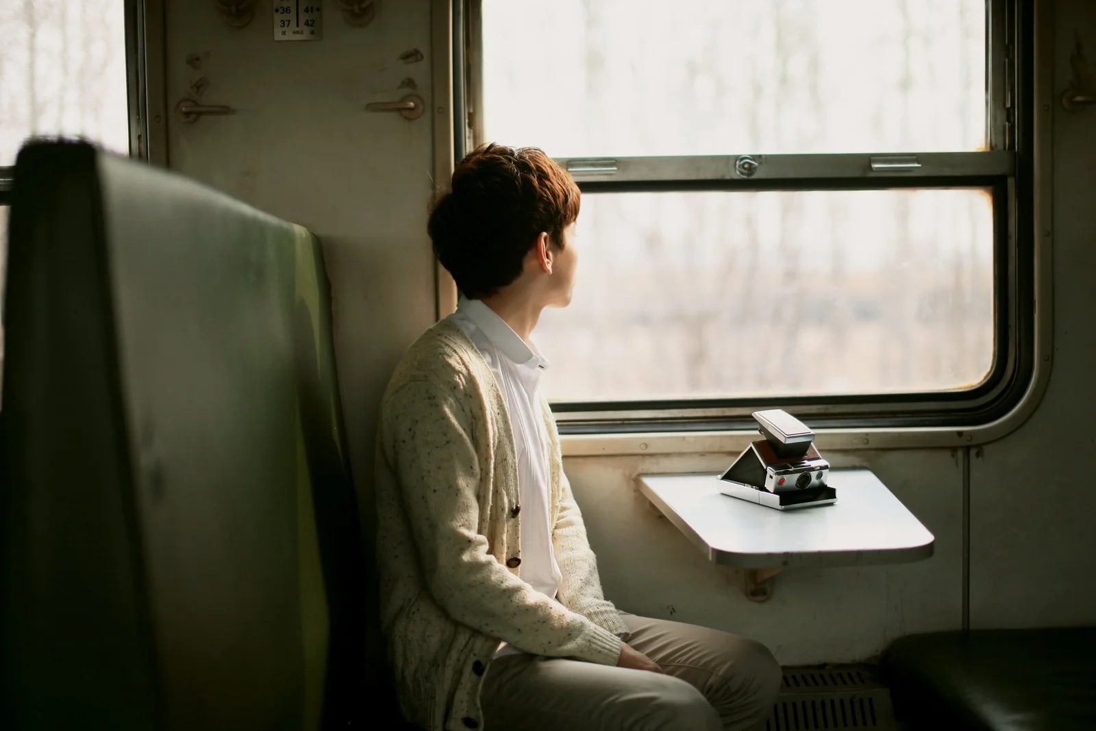 한 남성이 열차 좌석에 앉아 창밖의 밝은 풍경을 바라보고 있다.