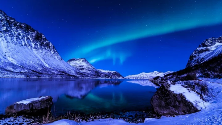 夜空下的绿色极光映照着被积雪覆盖的山脉与宁静湖面。
