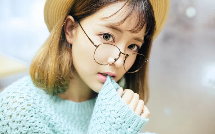 一名戴圆框眼镜和草帽的女子穿着浅蓝色针织衫近距离面对镜头。