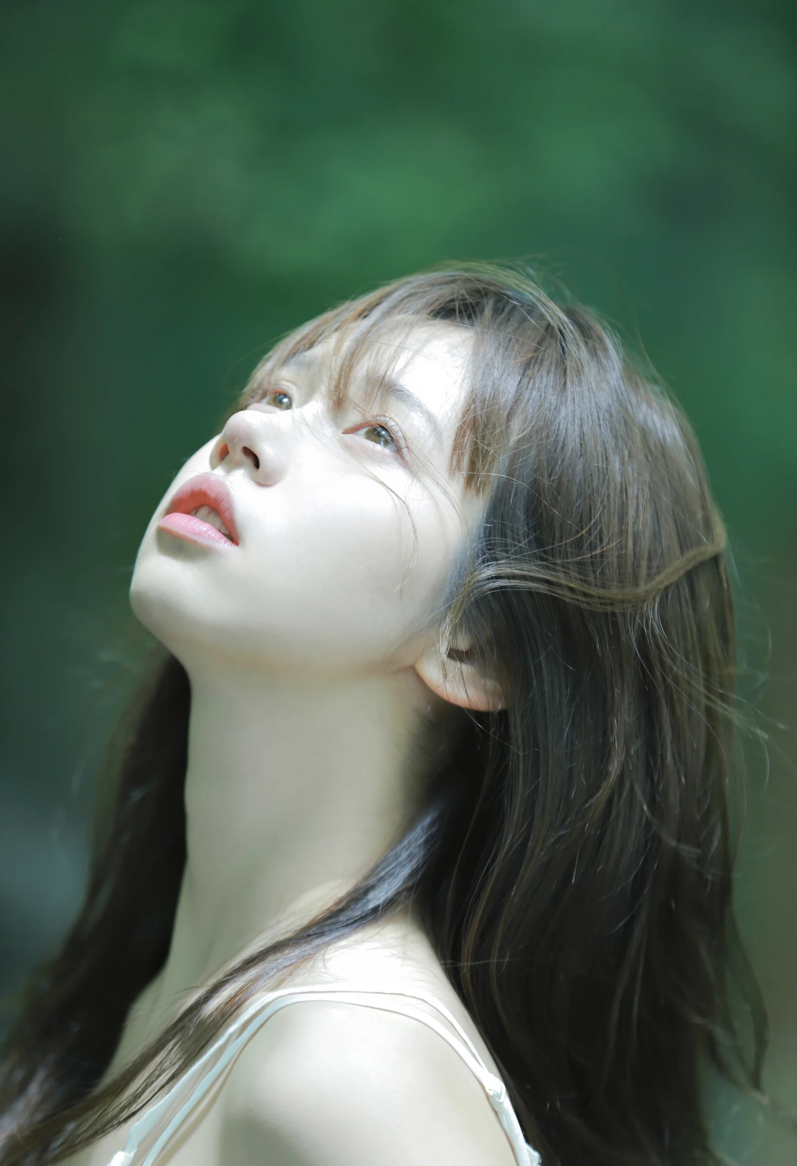 一名长发女性在绿色背景前抬头凝望，构成柔和的竖幅人像画面。