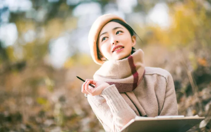 一位戴着围巾的女性在秋日户外手持笔记本微笑。