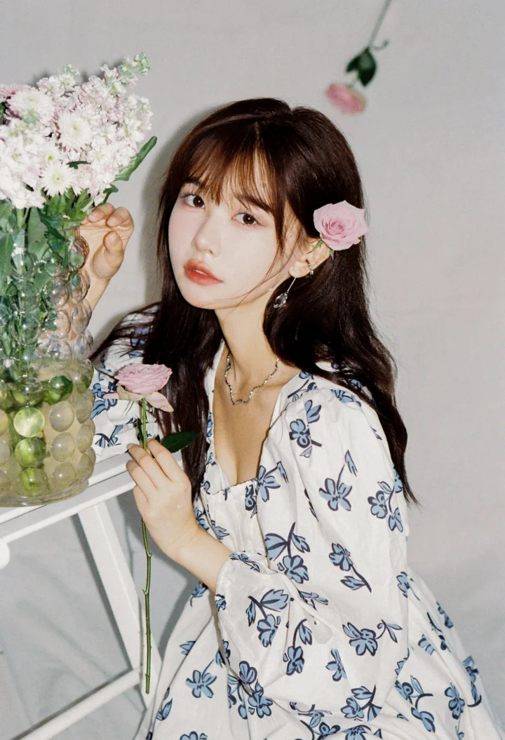 파란 꽃무늬 옷을 입은 여성이 꽃다발 옆에서 분홍색 꽃을 들고 있습니다.
