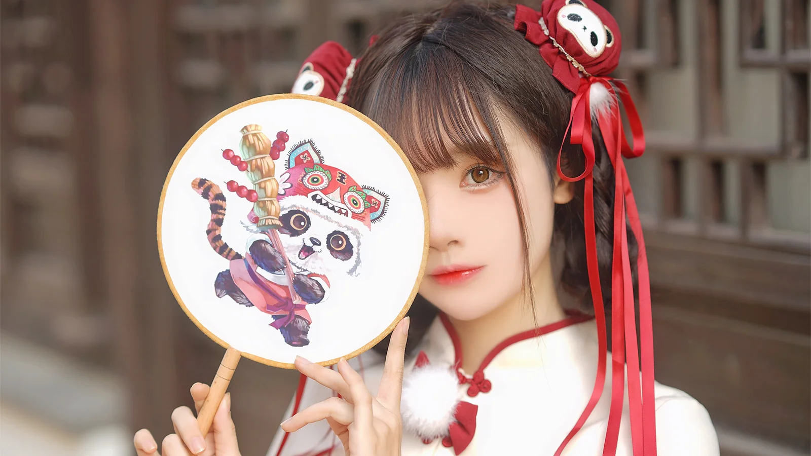 一名女性手持绣花圆扇，面部部分被扇子遮挡，红色发饰和飘带垂在两侧。