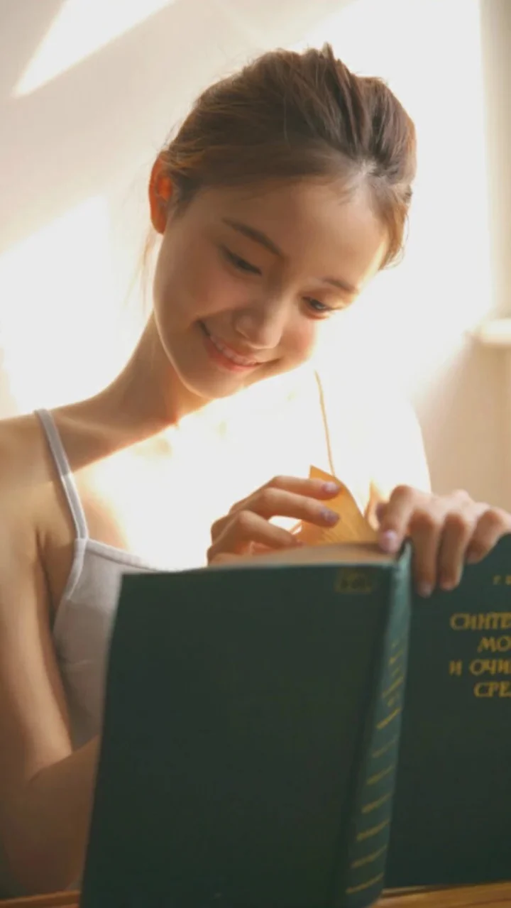 一名年輕女子在明亮的陽光下翻閱一本深綠色的書。