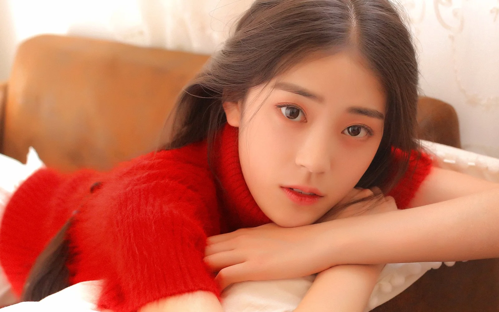 赤いセーターを着た女性がソファに伏せてカメラを見つめています。