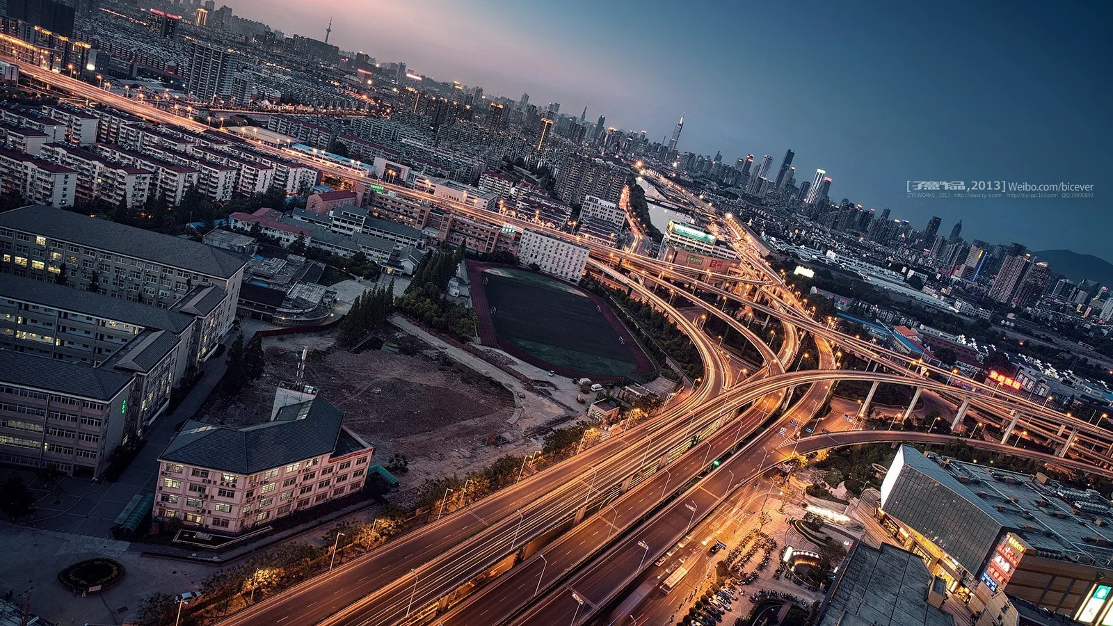 俯瞰夜幕下灯光交织的城市建筑群与多层立交道路。