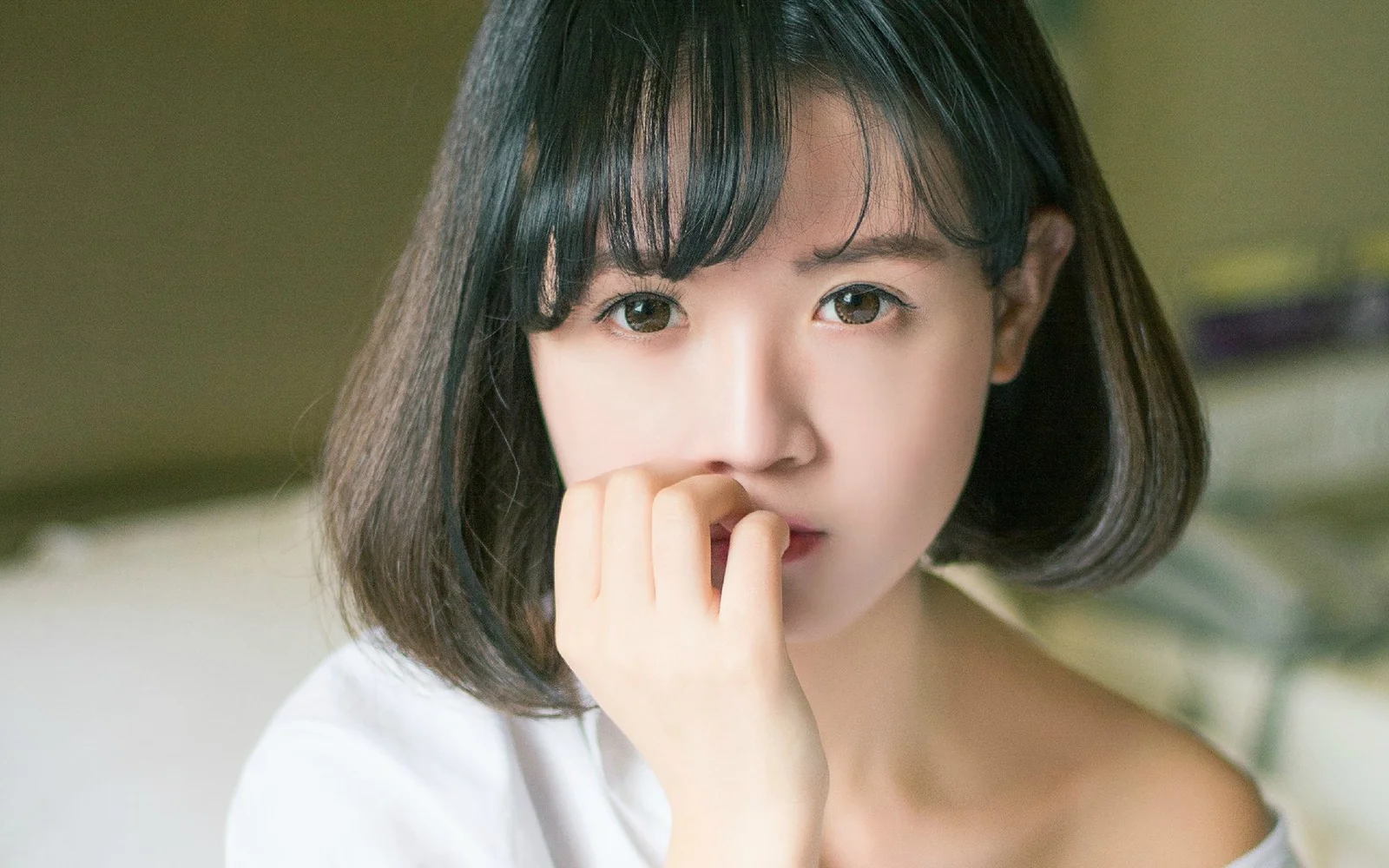 검은 단발머리 여성이 카메라를 바라보며 손가락을 입술에 살짝 댄 근접 인물 사진입니다.
