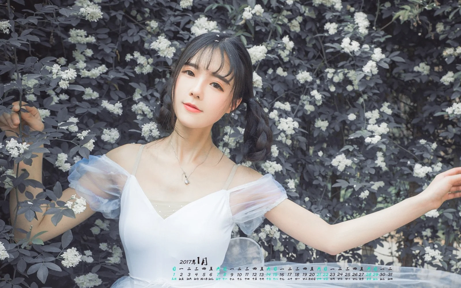 흰색 원피스를 입은 성인 여성이 흰 꽃이 핀 관목 앞에 서 있습니다.
