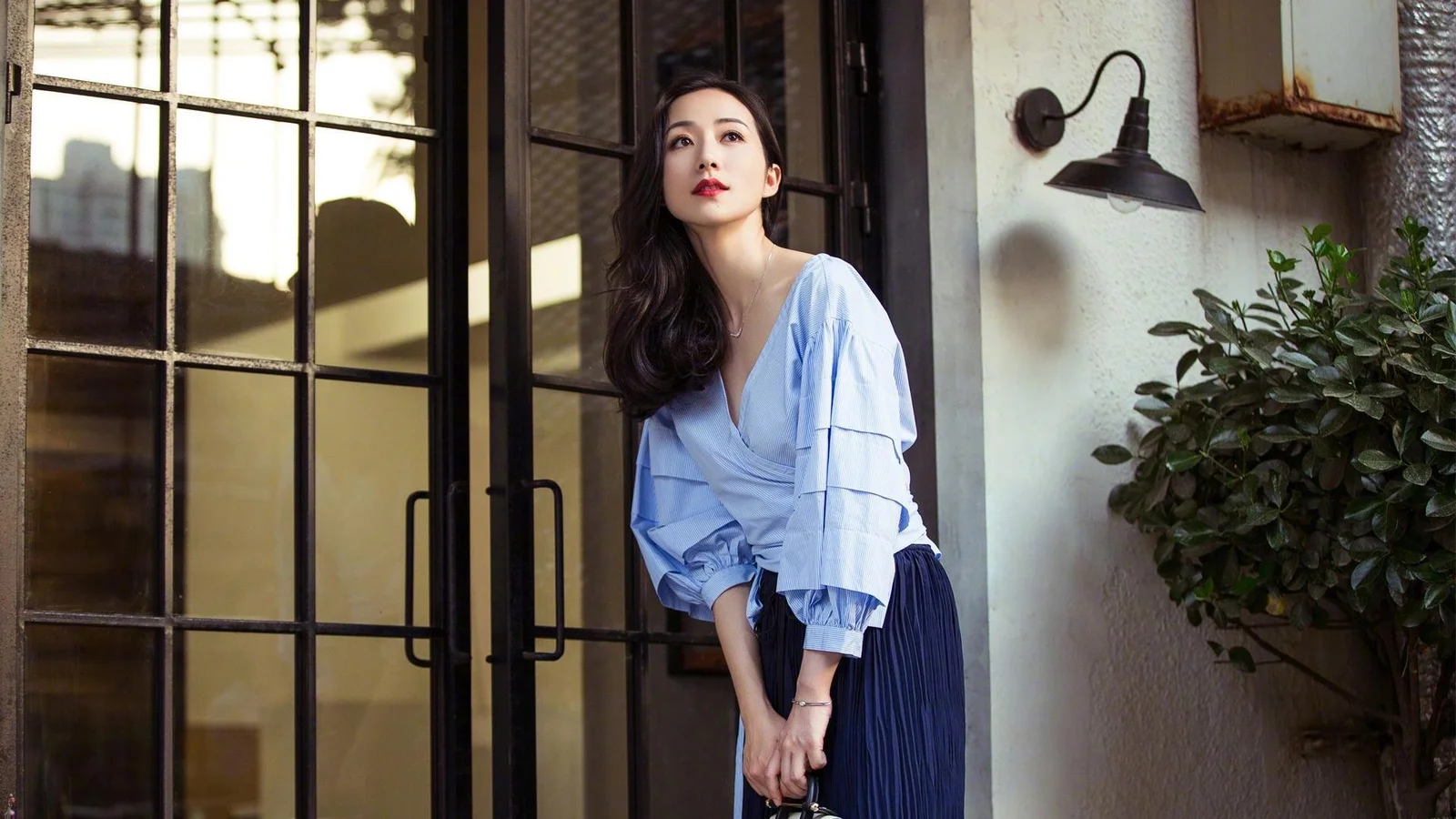 연한 파란색 블라우스를 입은 여성이 유리문 옆에 서 있습니다.