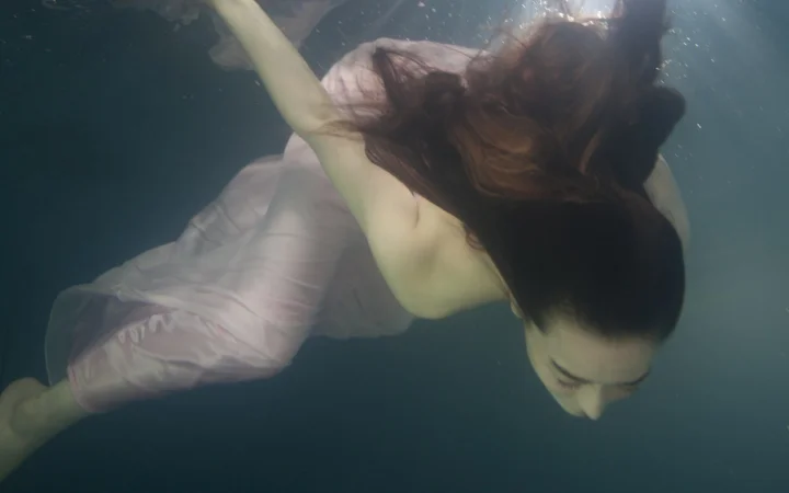 淡い色のワンピースを着た女性が水中を漂っている。