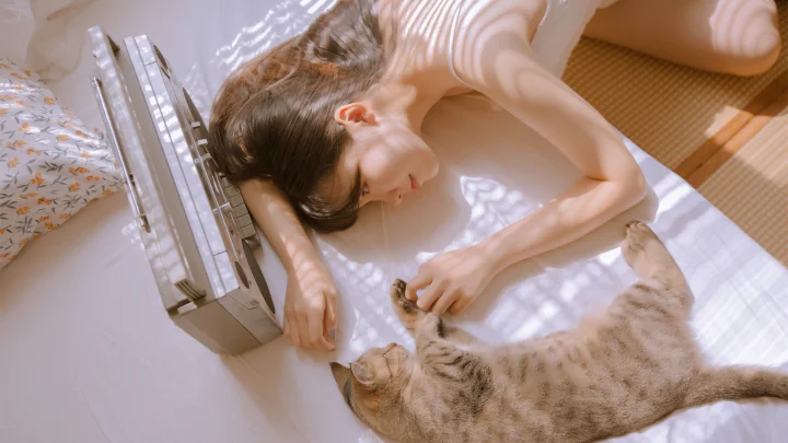一名女子躺在床上，在斑驳阳光下轻抚身旁的猫。