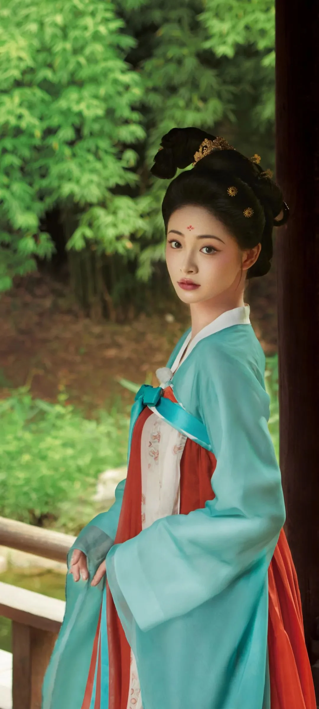 一名身穿青绿色传统服饰的女性站在竹林旁的木栏边。