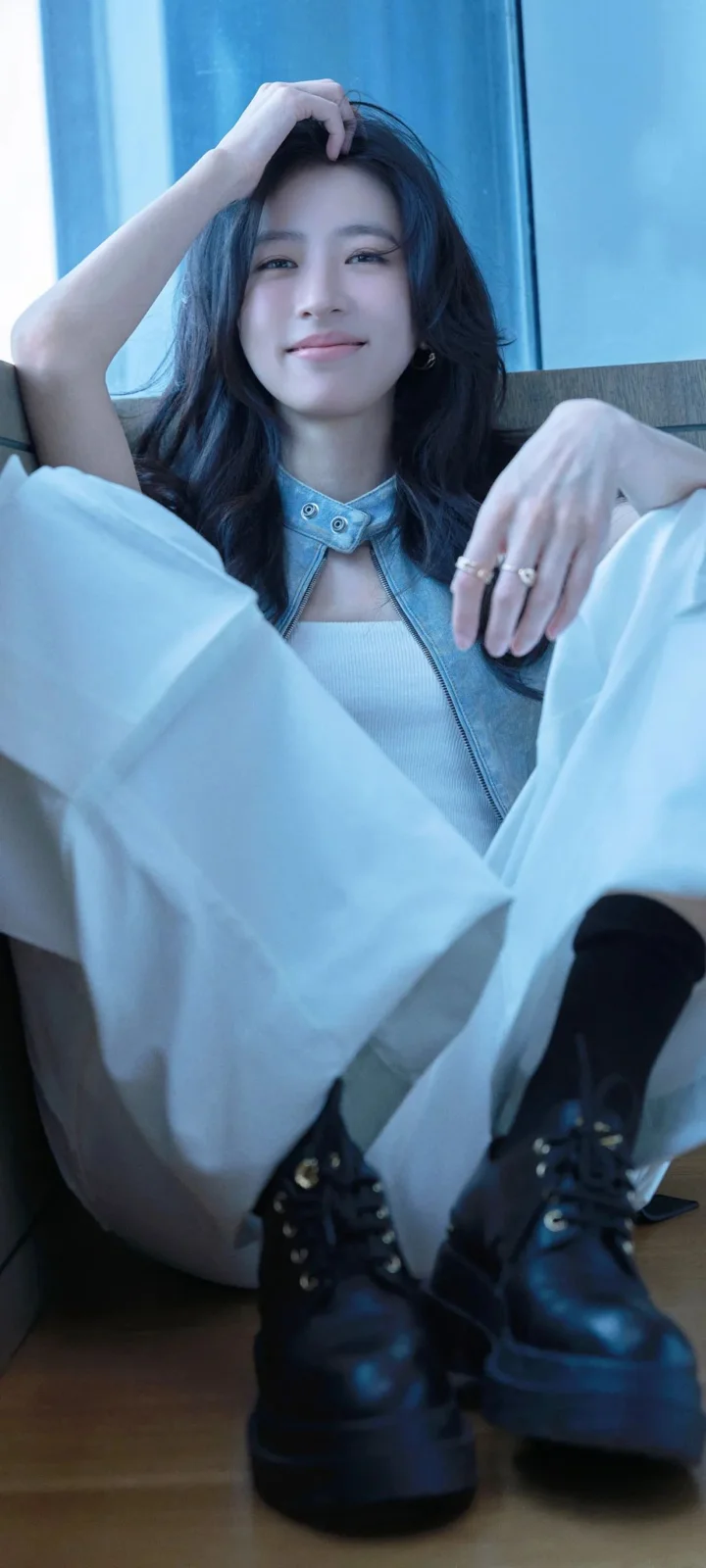 一名长发女性身穿浅蓝色服装坐在室内地板上，面向镜头微笑。