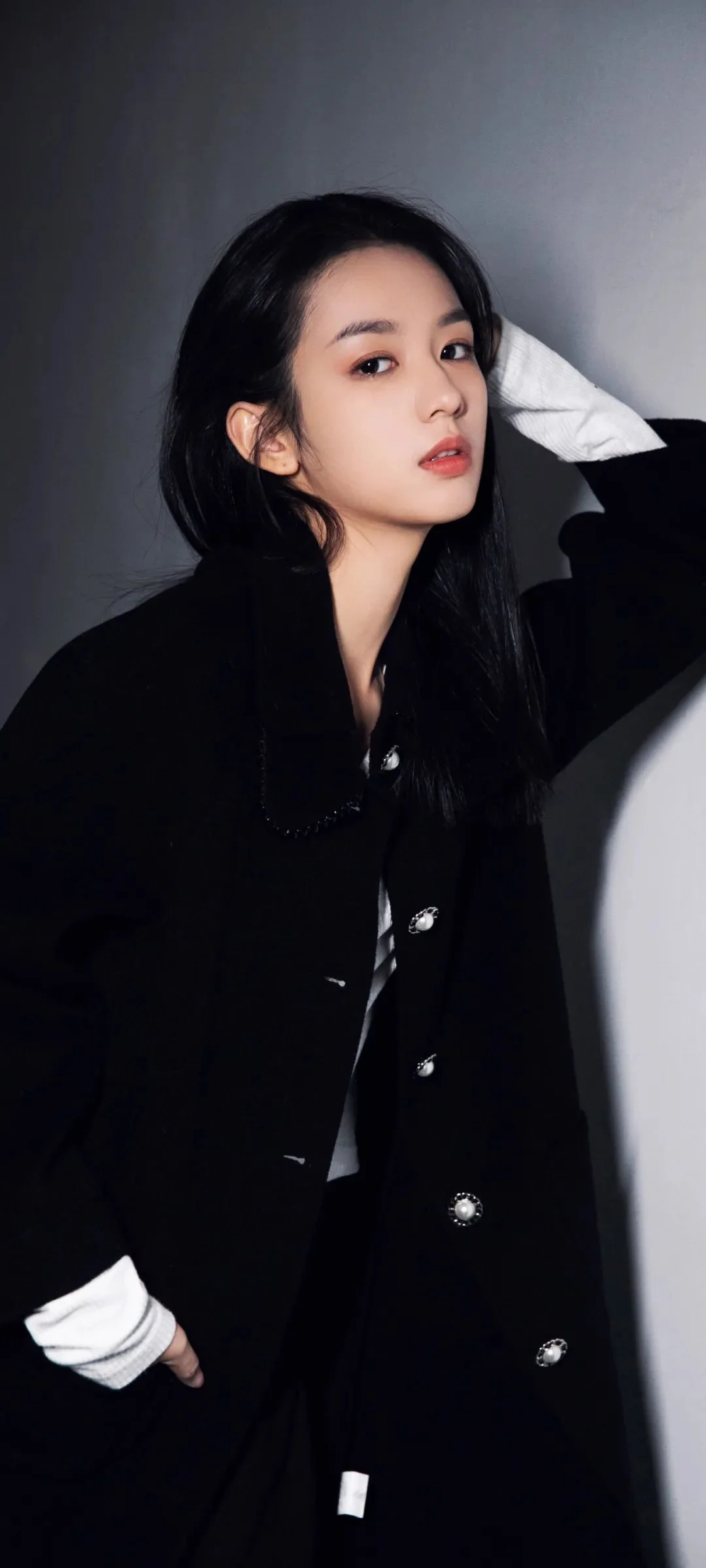 一名成年女性穿着黑色外套靠墙摆姿势。
