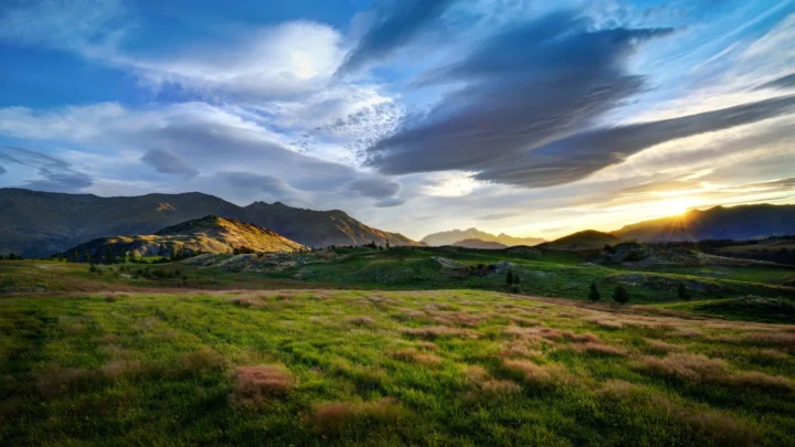 群山、草地与云层在夕阳下构成开阔的山谷风景。