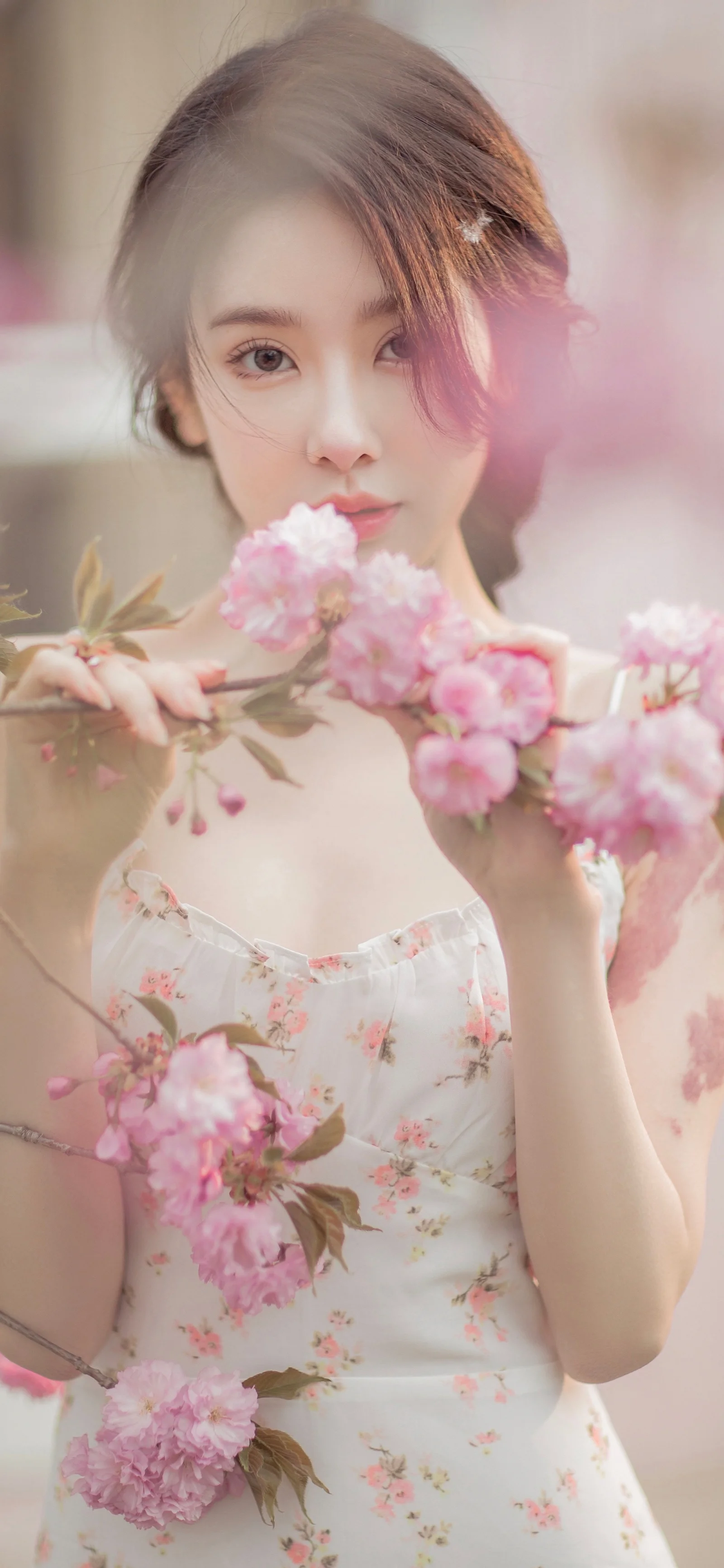 一位身穿碎花连衣裙的女性手持粉色花束面对镜头。