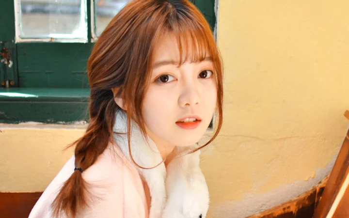 一名棕发女性在黄色墙壁和绿色窗户前看向镜头。