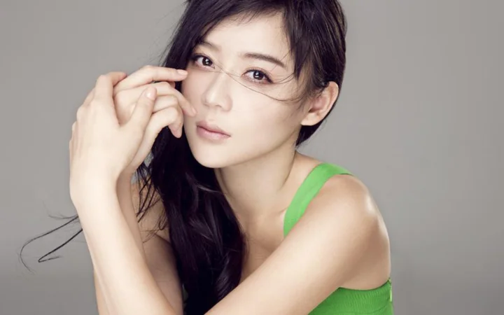 一名留着深色长发的女性在灰色背景前注视镜头，身穿绿色无袖上衣。