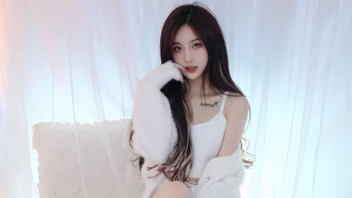 一名长发女性身穿白色服装坐在白色窗帘前，面向镜头。