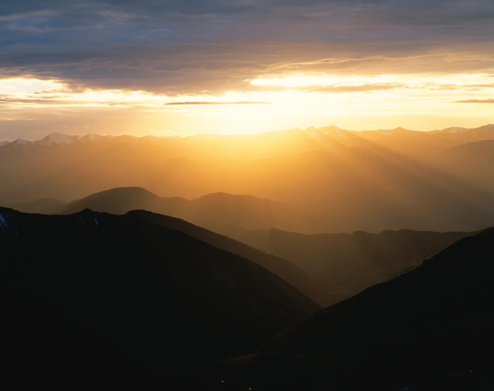 雲間から差し込む夕日が連なる山々を照らし、黄金色の夕景を作り出している。