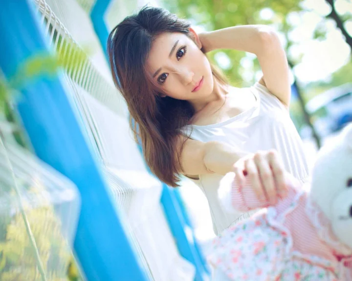 一名成年女性倚靠在户外白色栏杆旁，穿着白色上衣和花卉图案裙子。