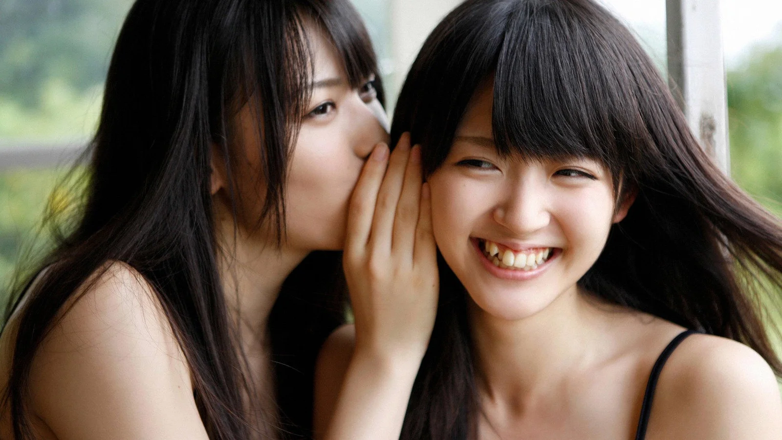 两名女性近距离面对镜头，其中一人微笑，另一人在她耳边低语。
