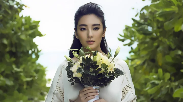 一名女子站在绿叶环绕的户外小径中，手捧一束花。
