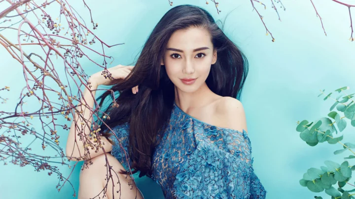 一位成年女子穿着蓝色露肩上衣，在浅蓝色背景和枝条前摆姿拍摄。